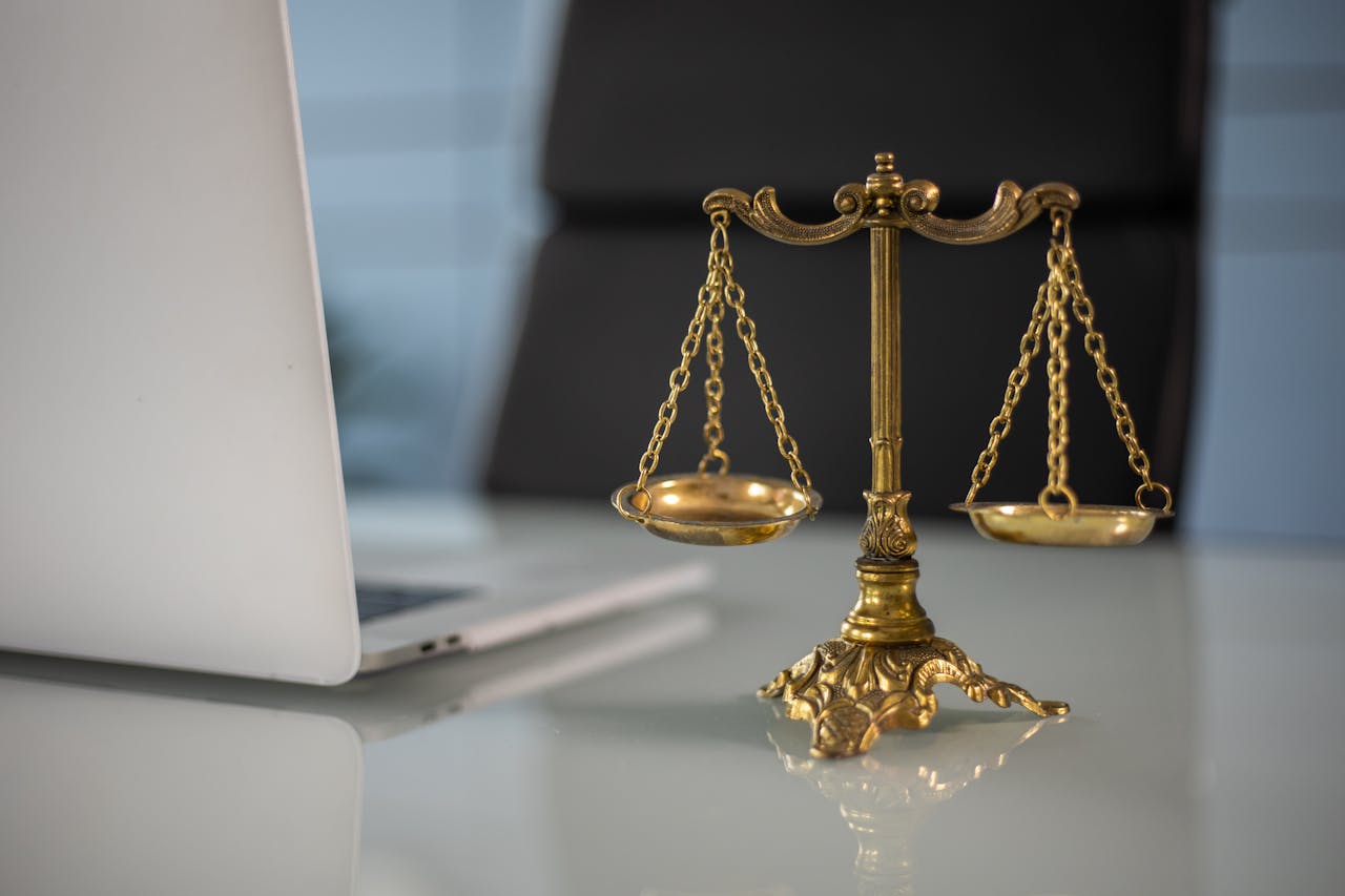 heros-img Golden justice scales on a desk beside a laptop, symbolizing law and balance.
